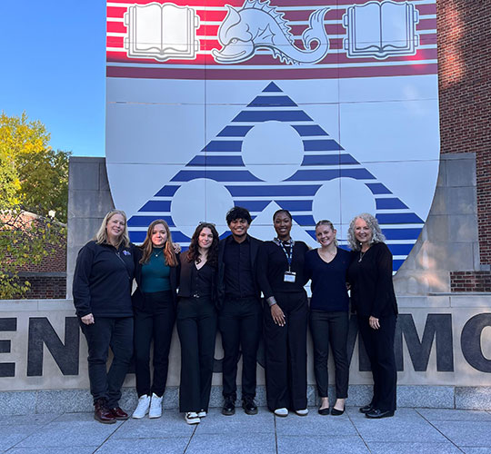 seven people standing in a line in front of a sign