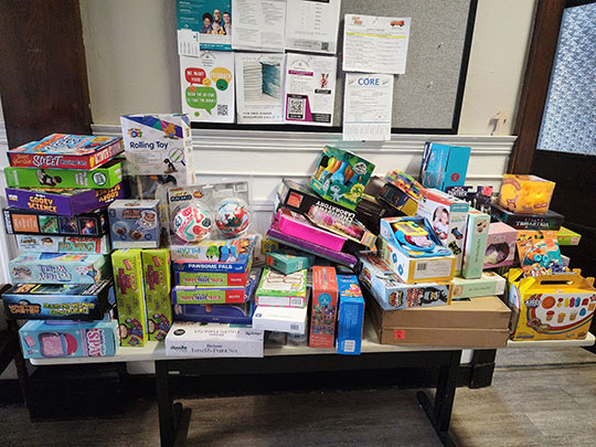 Stacks of toys and games on a table purchased with funds raised by the Alfred University Marketing Club for families in need.