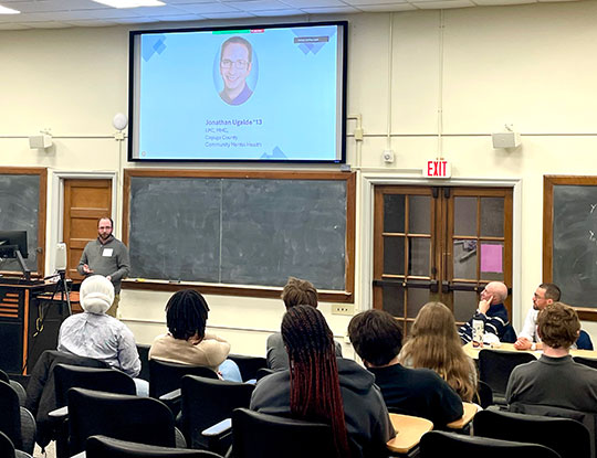 man standing in front of a projector, talking to some people