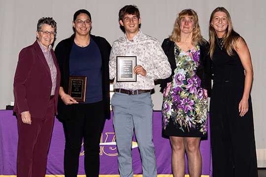five people standing in a row, two holding plaques