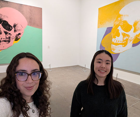 two women standing in a room in front of some art