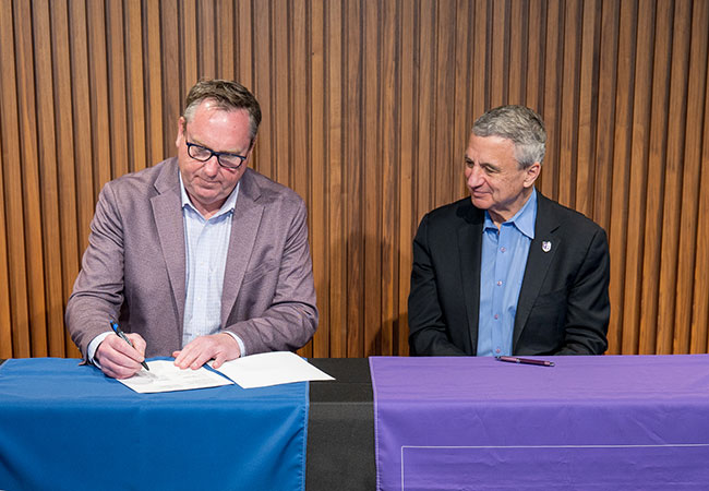 two people sitting at a table, one signing a document