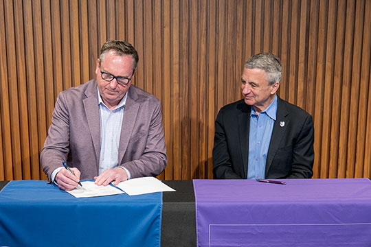 two people sitting at a table, one signing a document