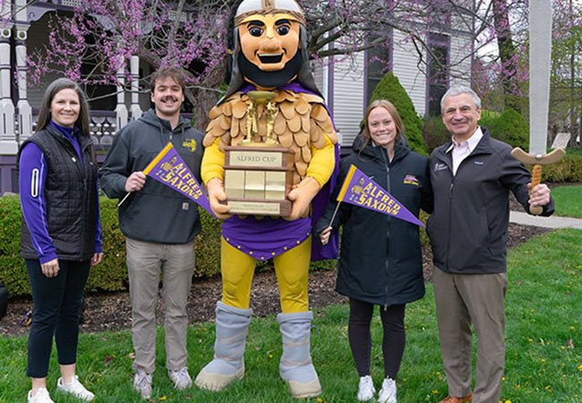 a mascot holding a trophy, flanked by four humans