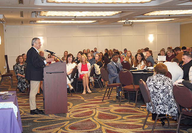 man at podium speaking to a large crowd