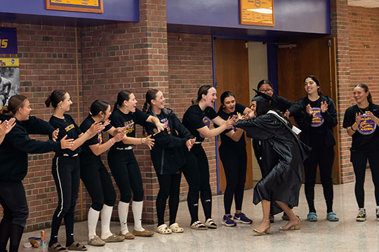 young women in cap and gown getting high fives from a group of young women