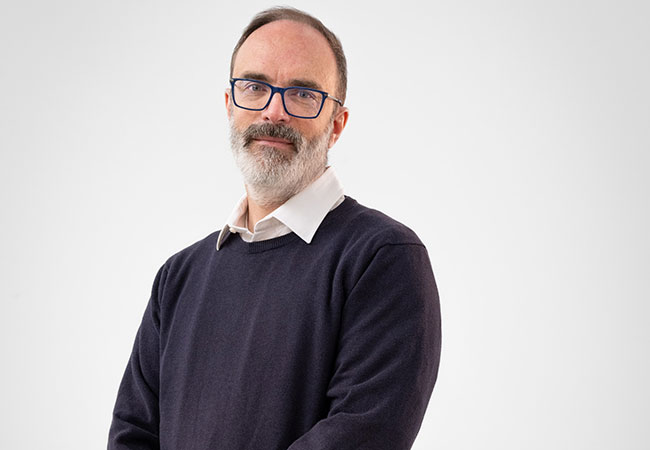 headshot of man in glasses, wearing sweater and collared shirt