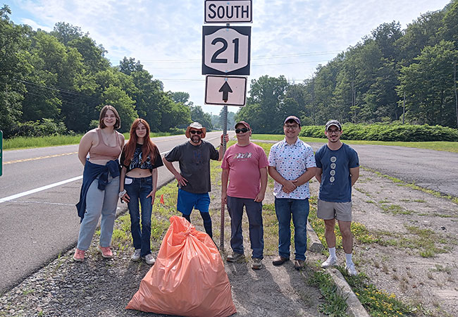group of people standing next to a road sign with a bag of trash in front of them