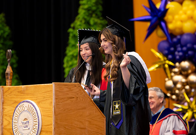 two young women in cap and gown at a podium