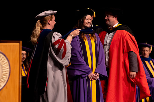 woman in cap and gown getting a hood placed over her head