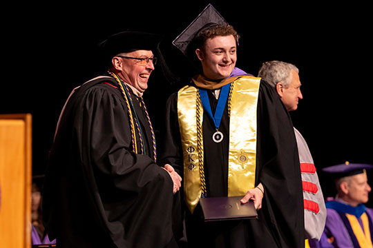 man in cap and down with diploma, standing next to someone else in a cap and gown