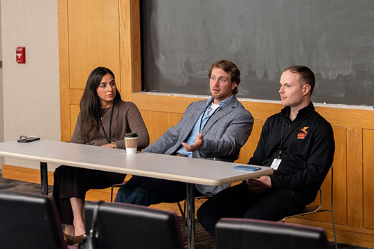 three people sitting at a table, one talking