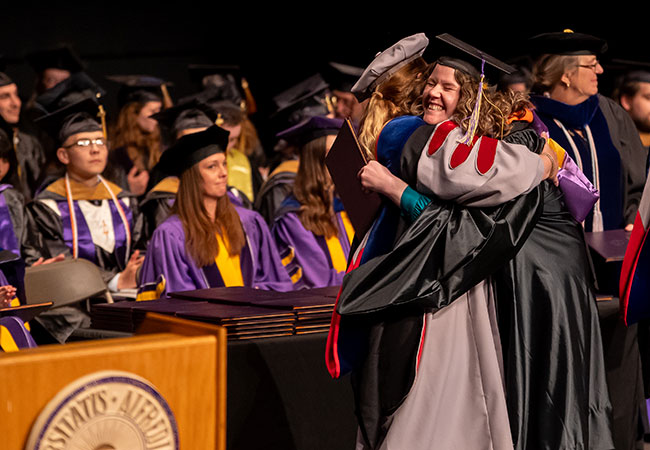woman in cap and gown hugging someone else in a cap and gown