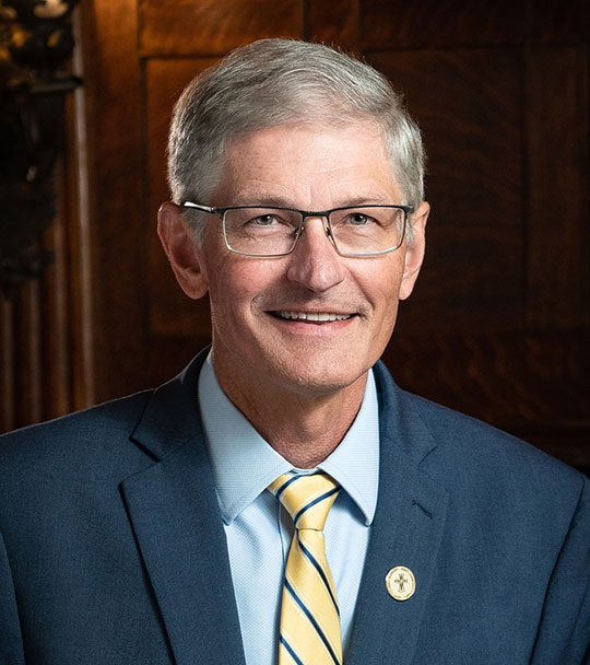 headshot of smiling man with glasses in suit and tie
