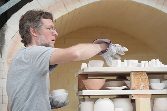 man working on some ceramic art pieces by a kiln