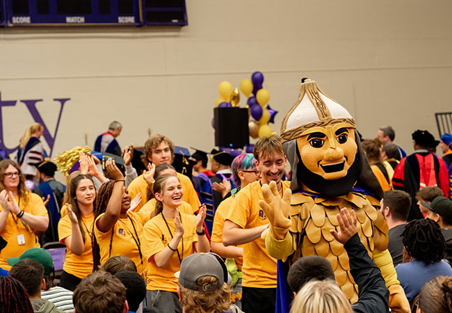mascot leading a procession of students through a crowd