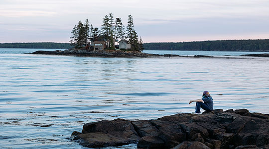 photo of a woman sitting on the beach with an island cottage in the background