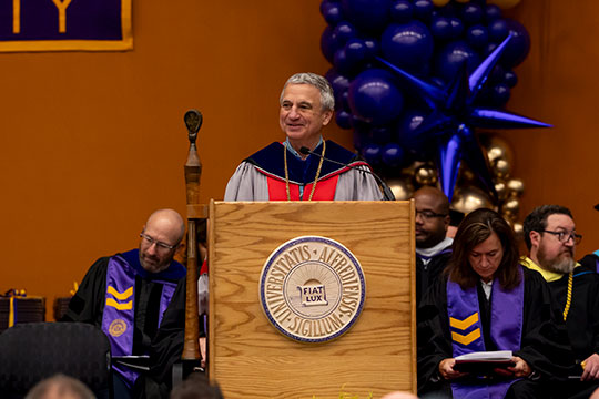 man in a gown talking at a podium