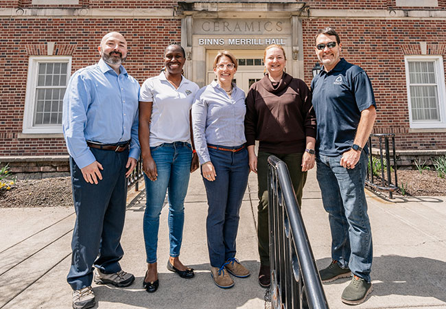 five people standing in front of a brick building
