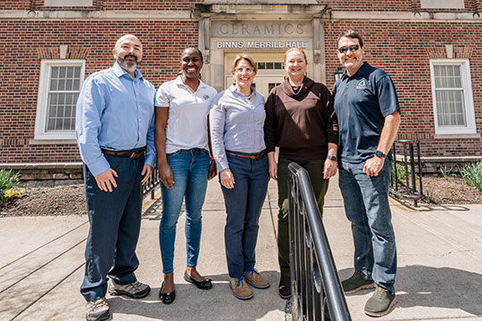 five people standing in front of a brick building