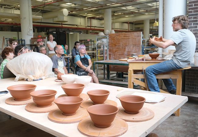 man talking to a group of people with ceramic art on a table