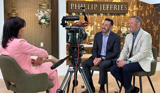two men being interviewed by a woman, TV camera in foreground