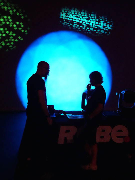 two people standing in front of bright blue lighting, silhouetted