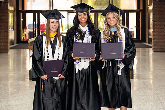 three young women in caps and gowns holding diplomas