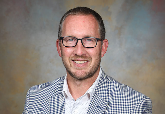 headshot of man in blazer and dress shirt wearing glasses