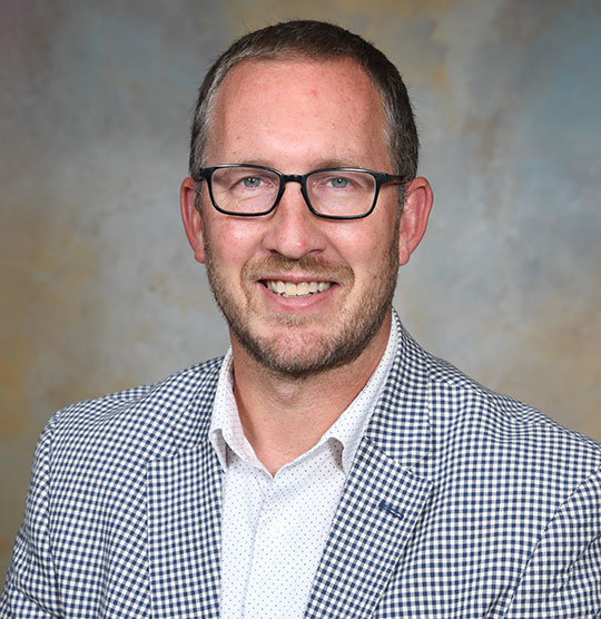 headshot of man inblazer and dress shirt wearing glasses
