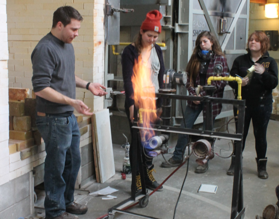 Students working with glass in the hotshop in front of a gas furnace