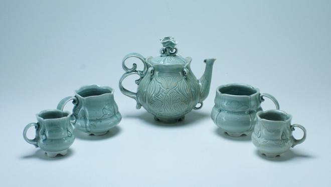A carved celadon tea set including a teapot centered between two large cups and two small cups. 