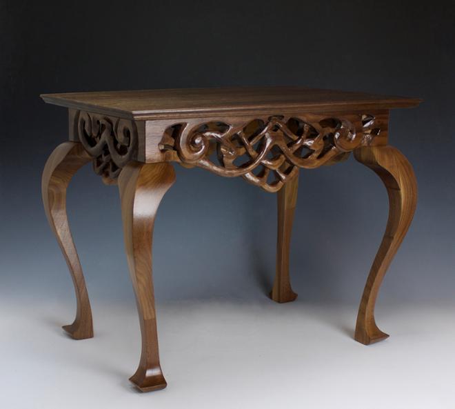 A lacquered, dark wood tea table with carved lattice skirt boards, and Queen Anne’s legs. 