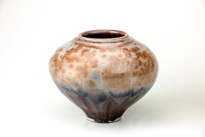 A bulbous crystalline vase form.  From the top of the vase, the color of crystals fades from variations of tan and lilac to purple then to matte black at the bottom of the foot.  