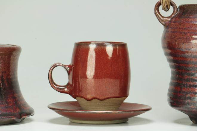 A bright, luscious red mug sits on top of a matching saucer in the middle of the photo, to the left is the side of a jar, and to the right the side of a vase.  