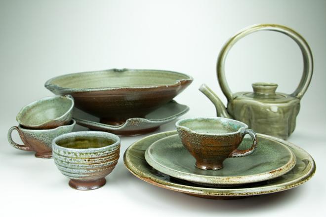 A collection of functional soda-fired pottery with green celadon glazes.  The collection includes plates, bowls, a cup, teacups, and a teapot.  