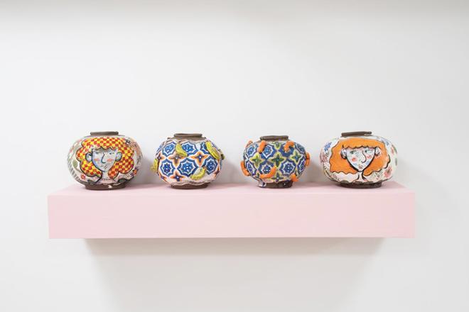 Four round pots in a row on a pink shelf. The center pots are decorated with Cheetos and bananas and the pots on the outside have women’s faces. 