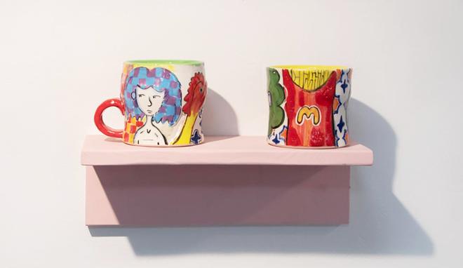A view of four mugs, each on a different pink shelf. The Mugs are decorated with bright colors.