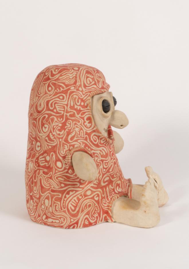 A heavily patterned smiling creature covered in intuitively placed red designs. Stoneware and underglaze.