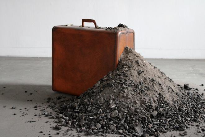 Brown leather suitcase on ground with pile of ashes piled on side.