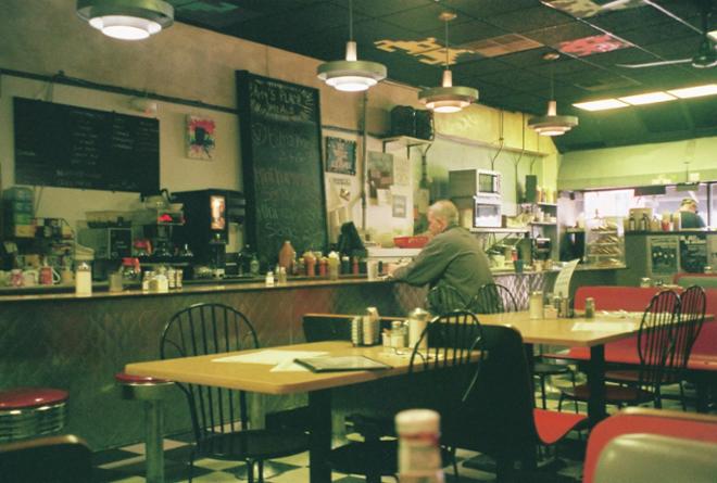 A photograph of a man sitting at the bar in a diner. 