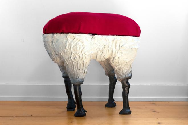 A stool with a red cushion and the legs of a sheep. 