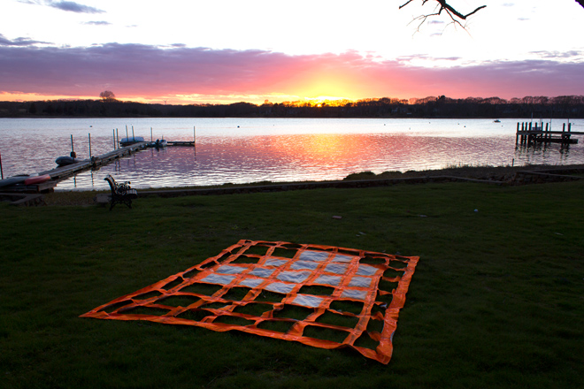orange tarp with square holes on green grass by a lake during sunset