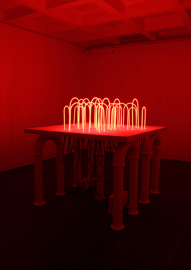 neon glass u-shaped red lights upside down on a table with ceramic pipe legs
