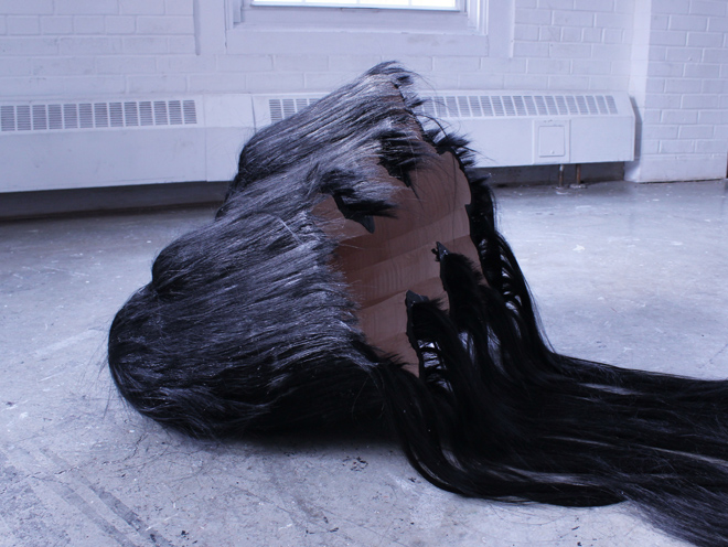 ceramic sculpture on the floor with black and grey hair glued to it and draping off of it.