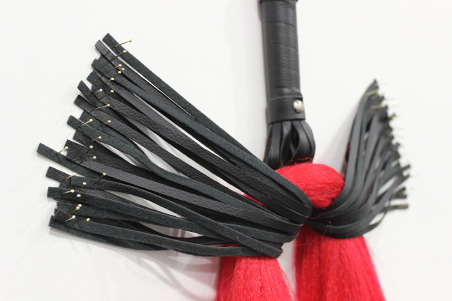 red hair hanging from a leather flogger pinned to the wall