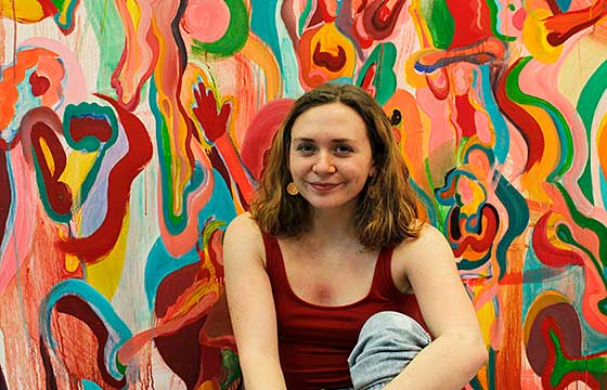 smiling woman sitting in front of large colorful painting