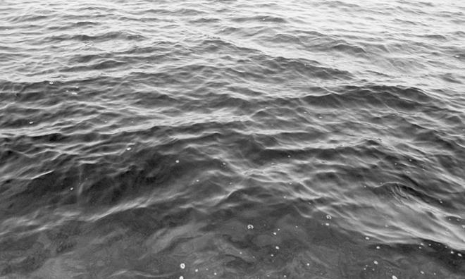 A black-and-white photograph depicting the surface of water with some small waves and bubbles.