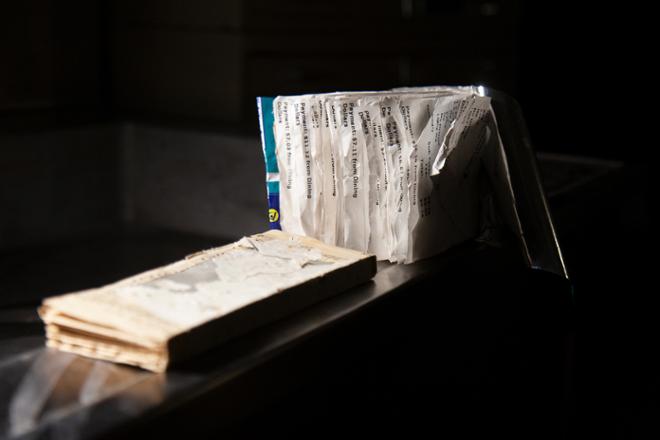 Starkly lit in a dark room, two artist books balance on the edge of a sink. One is made of collected receipts and bound in a chip bag. The other is aged paper.