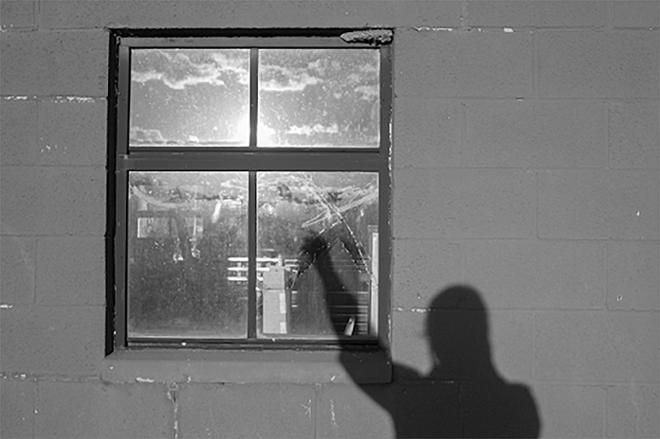 A photograph of a person's shadow reaching at the reflection on a window.  